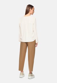 Hellbeige Bluse mit langen Ärmeln und rundem Ausschnitt, kombiniert mit lockeren, hellbraunen Hosen und weißen Plateauschuhen.