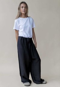 Ontspannen zwarte linnen broek met een trekkoord in de taille, gecombineerd met een eenvoudig wit katoenen T-shirt. De outfit heeft een casual ontwerp.