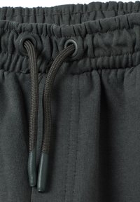 Donkergrijze trainingsbroek met een gathering elastische tailleband. Voorzien van decoratieve koordjes met groene plastic uiteinden. Zacht, gemêleerd stof.
