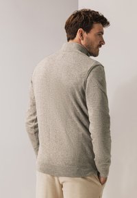 Hellgrauer Strickpullover mit hohem Kragen, figurbetontem Design und gerippten Bündchen. Hergestellt aus einem weichen Material, das eine dezente Textur aufweist.