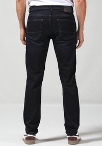 Jeans de mezclilla oscura con un corte recto, detalles de costura en contraste y dos bolsillos traseros, combinados con zapatillas casuales.