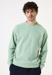Sudadera verde claro con cuello redondo y mangas raglán. Confeccionada en una tela suave, presenta un acabado texturizado y una etiqueta de logo sutil en el dobladillo.