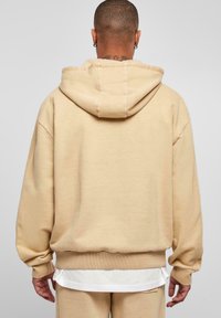 Beige kapucnis pulóver laza fazonban, bordázott mandzsettákkal és aljjal, puha tapintással, és elülső kenguruzsebbel.