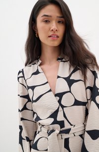Beige wrap dress with a black abstract pattern, long sleeves, and a belted waist. Soft fabric with a textured finish and collar detail.