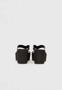 Černé platformové sandály s hladkým povrchem, vybavené širokým zadním páskem a silným, chunky podpatkem. Jednoduchý design s minimalistickými akcenty.