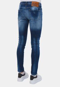 Slanke blauwe jeans hebben een vervaagd ontwerp met versleten gebieden, vijf zakken en een tan leren label bij de tailleband. Gekocht met witte sneakers.
