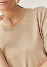 Béžový pletený sveter s okrúhlym výstrihom. Mäkká textúra, krátke rukávy a rebrované manžety. Čisté línie a minimalistické dizajnové detaily.