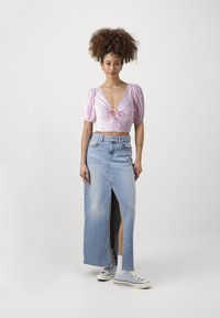 Rosa kort topp med puffärmar och knytdetalj, tillsammans med en högmidjad denimmaxikjol med en sidoknapp, bärs med blå sneakers.