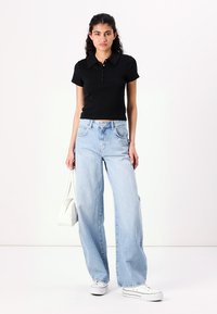 Svart kortärmad polo, ljusblå vida jeans, vita sneakers och en vit handväska. Släta material, avslappnad passform och klassisk design.