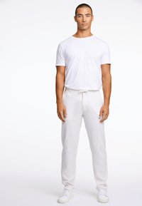 White cotton t-shirt paired with light linen pants. Pants feature a drawstring waist. Model wears white sneakers, standing against a plain background.