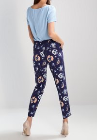 Světle modrý top s krátkým rukávem spárovaný s tmavě modrými kalhotami se květinovým vzorem, které mají broskvové a bílé akcenty. Kalhoty mají přiléhavý střih.