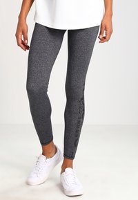 Grå leggings med en melerad textur, med en figursydd design och sidobrandingdetaljer, kombinerat med vita sneakers och en lös vit topp.