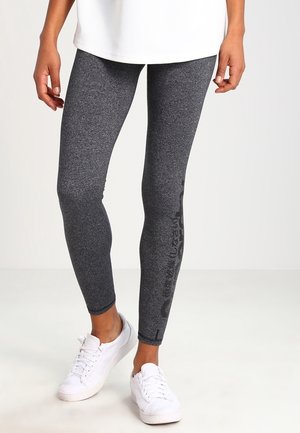 Grijze leggings met een gemêleerde textuur, voorzien van een aansluitend ontwerp en zijkantbranding, gecombineerd met witte sneakers en een losse witte top.
