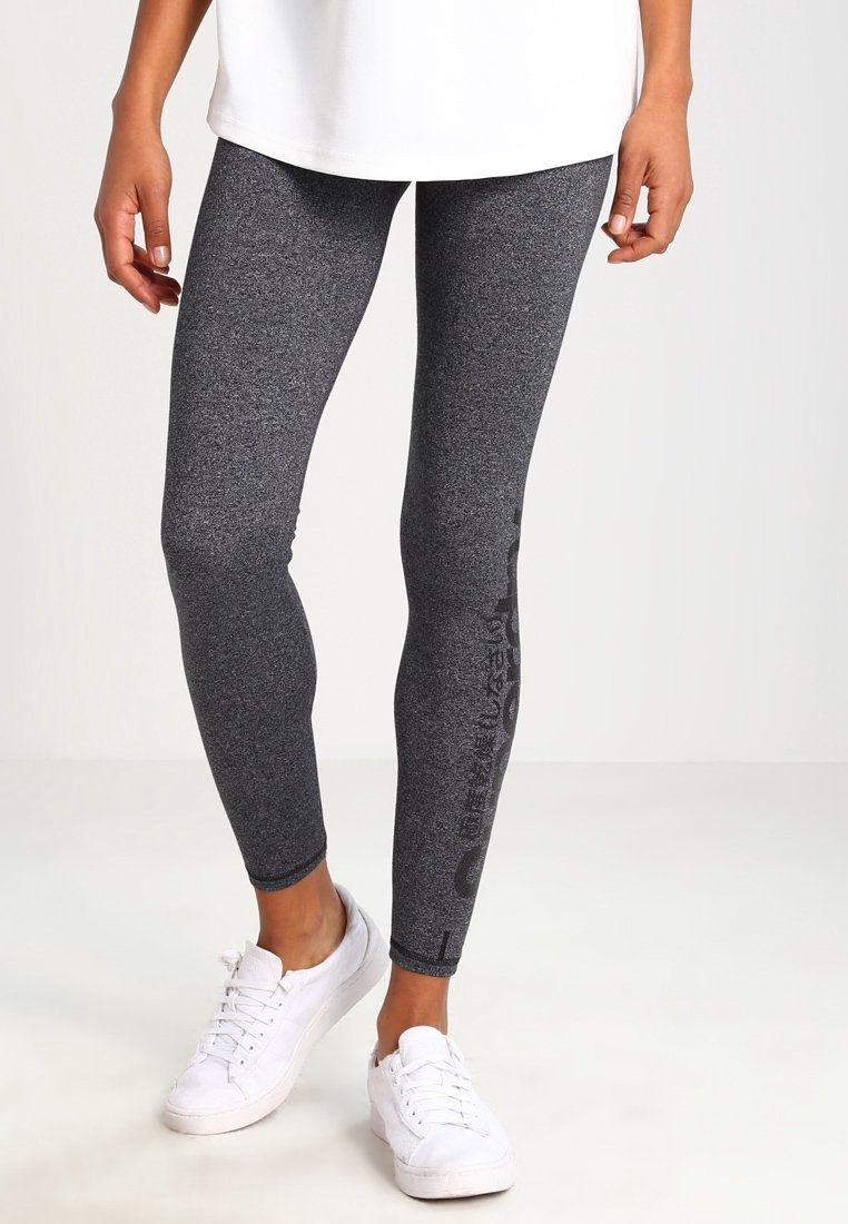 Grå leggings med en melerad textur, med en figursydd design och sidobrandingdetaljer, kombinerat med vita sneakers och en lös vit topp.