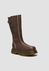 Pruun nahast poolkõrge saabas paksu läbipaistva tallaga, roosa äärega esiküljel ja taga ning külje peal reguleeritav rihm metallist pandlaga.