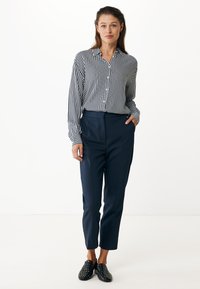 Striped, button-up shirt in navy and white; paired with tailored navy trousers; black slip-on shoes with white polka dots; smooth texture.