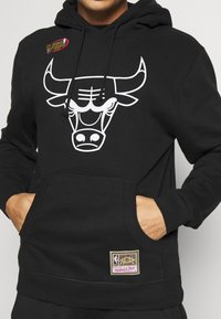 Svart hoodie med en vit tjur grafik på framsidan, framficka och en etikettpatch på den nedre sidan. Mjuk, texturerad tyg.