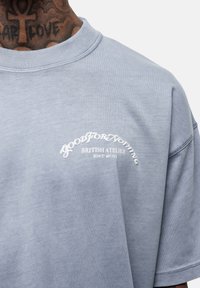 Niebieska bawełniana koszulka oversize z okrągłym dekoltem. Posiada biały nadrukowany tekst: "GOOD FOR NOTHING BRITISH ATELIER EST 2011." Miękka tekstura.