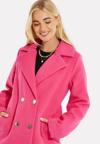 Cappotto in misto lana fucsia con colletto a rever, design doppiopetto, due tasche anteriori e grandi bottoni decorativi.