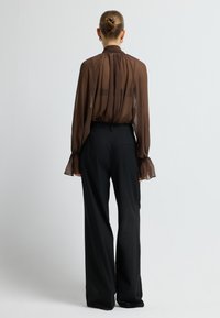 Braune transparente Bluse mit gerafftem Ausschnitt und Glockenärmeln, kombiniert mit hochtailierten schwarzen weit geschnittenen Hosen mit einer Gesäßtasche.