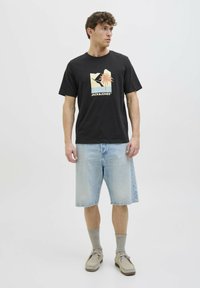 Camiseta de algodón negra con un estampado gráfico que presenta una palmera, combinada con pantalones cortos de mezclilla azul claro y calcetines grises. Se incluyen calzado informal.