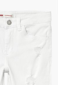 Vaqueros de mezclilla blanca con un corte super ajustado, que presentan desgastes y rotos, hardware de botón plateado y un clásico diseño de cinco bolsillos.
