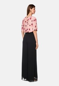 Floral, kurzärmlige Bluse in Pink mit schwarzen Akzenten, kombiniert mit hoch taillierten, weiten schwarzen Hosen. Glatte Texturen überall.