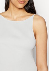 Top de alças finas, em tom cinza claro, com textura canelada e decote arredondado. Vista em close que destaca os detalhes do tecido.