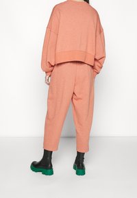 Pink cropped sweatshirt and matching wide-leg pants, featuring soft texture. Paired with black platform boots with green sole accents.