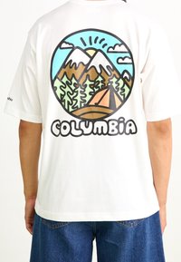 Camiseta de algodón blanca con un gráfico colorido de montañas y bosque en la parte trasera. "COLUMBIA" está escrito en letras negras y en negrita debajo.