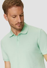 Jasnozielona koszulka polo wykonana z bawełny. Posiada klasyczny kołnierzyk, zapięcie na dwa guziki oraz subtelną strukturę materiału.