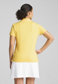 Polo shirt giallo a maniche corte con colletto a costine, caratterizzato da una texture liscia e un design aderente, abbinato a una gonna bianca.