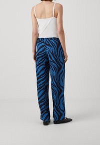 Blue zebra print wide-leg pants with a comfortable elastic waistband, featuring a smooth fabric texture and relaxed fit. Black flat shoes visible.