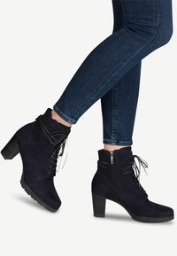 Botines de ante azul marino con tacón grueso, cordones en la parte delantera y cremallera lateral. Superficie texturizada y detalle de costura reforzada.