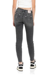 Jeans skinny in denim grigio scuro, con tasche posteriori decorate con cuciture distintive e un'etichetta con marchio. Abbinati a sneakers bianche e nere.