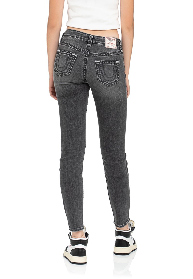 Jeans skinny in denim grigio scuro, con tasche posteriori decorate con cuciture distintive e un'etichetta con marchio. Abbinati a sneakers bianche e nere.