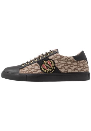 Lavtop sneaker med beige monogrammønster, sort læder tå og hæl, guldfarvede øjer og broderet rød og gylden våbenskjold på siden.