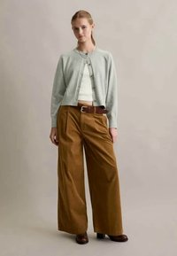 Cárdigan verde claro con escote redondo y botones, combinado con pantalones de pana marrones de pierna ancha de cintura alta y botas marrones.