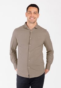 Camicia a maniche lunghe di colore verde oliva chiaro, modello con bottoni sul davanti, tessuto morbido, logo discreto sul petto, abbinata a jeans scuri.