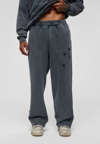 Grijze sweatpants met een comfortabele pasvorm, elastische tailleband en versleten details op het linkerbeen, gemaakt van zachte, gestructureerde stof.