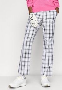 Triibulised golfipüksid musta ja valge värviga, kergest materjalist, lõdva silueti ja küljetaskutega. Kanda roosa sviitriga ja valgete kingadega.