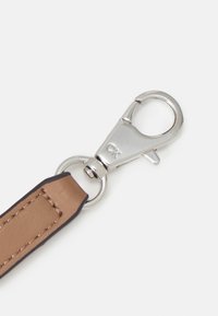 Bracelet en faux cuir marron avec des bords foncés, featuring un fermoir à pince en métal argenté, détaillé avec la lettre "CK" sur le matériel.
