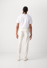 T-shirt blanc associé à un pantalon en lin crème et des baskets blanches. Le pantalon a une coupe droite et des détails de poche arrière.