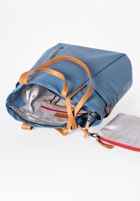 Zaino in pelle blu con spallacci beige, aperto per mostrare un interno grigio a motivo e una piccola pochette rossa con zip accanto.