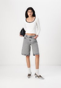Svart og hvit avkortet genser, høy midje denimshorts og metalliske sko. Modellen holder en svart håndveske, hvite sokker synlige.