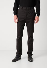Zwarte op maat gemaakte broek met een gladde textuur, met een klassiek ontwerp, knoopsluiting en zijzakken, gedragen met zwarte nette schoenen.