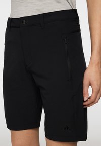 Mustat shortsit kevyestä materiaalista, joissa on vetoketjullinen tasku, vyölenkit ja pieni logotaito alaosassa.