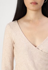 Helligem beige Pullover mit tiefem V-Ausschnitt, langen Ärmeln und einer weichen Textur, die subtile Farbvariationen aufweist.