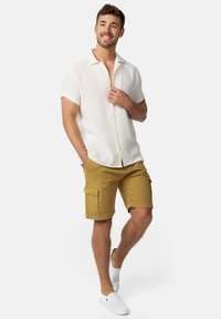 Let letan hvid kortærmet skjorte med en tekstureret finish, parret med sennepsgule cargo shorts med sidelommer og hvide slip-on sko.