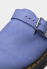 Κοντινή λήψη ενός μπλε σουέντ παπουτσιού με ασημένιο λουράκι με αγκράφα και κίτρινη ραφή σε μαύρη σόλα.